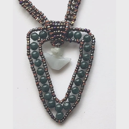 The medallion is made with jade beads in a triangle shape with a jade charm suspended in the middle. The necklace strands are made of intricately woven dark seed beads for a shimmering effect. 
