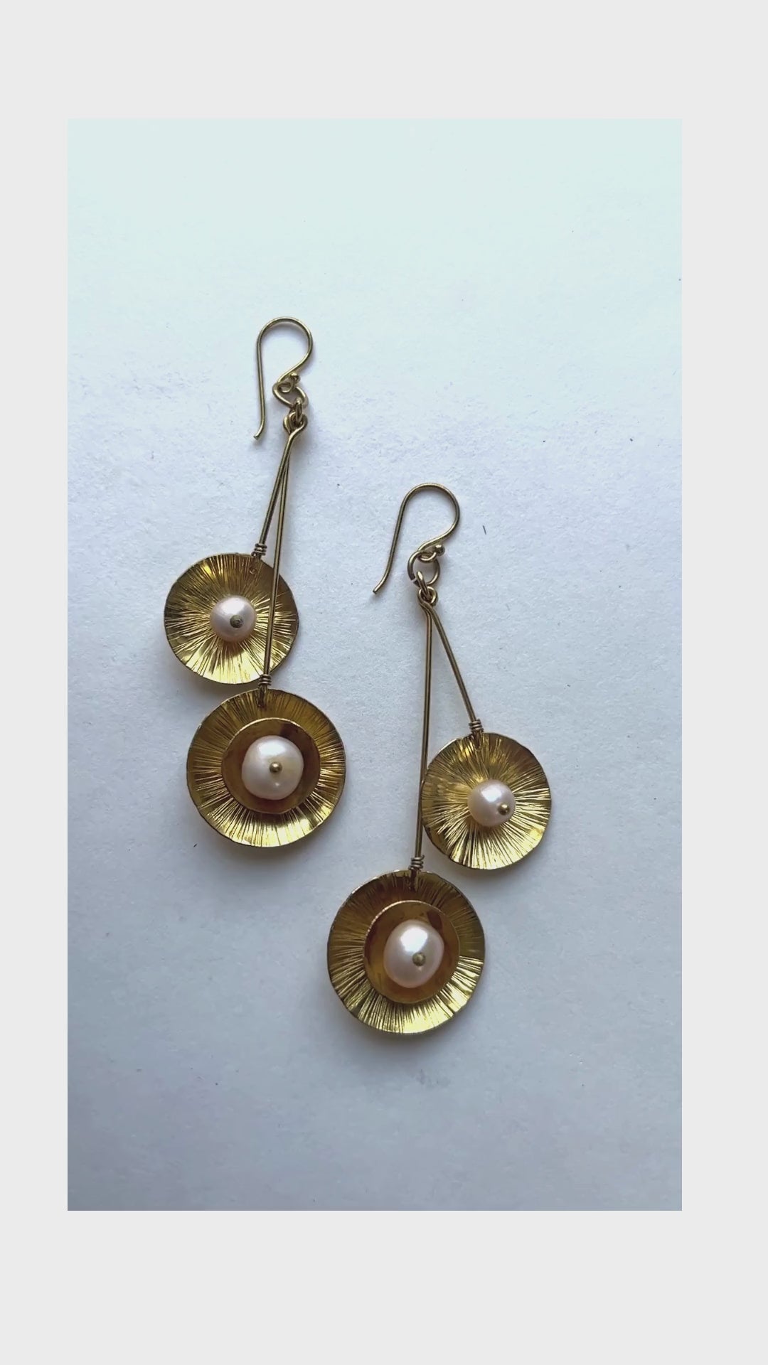 These dangling earrings have a unique design with a double drop with a round organic shape suspended at the bottom containing a pearl in the middle.