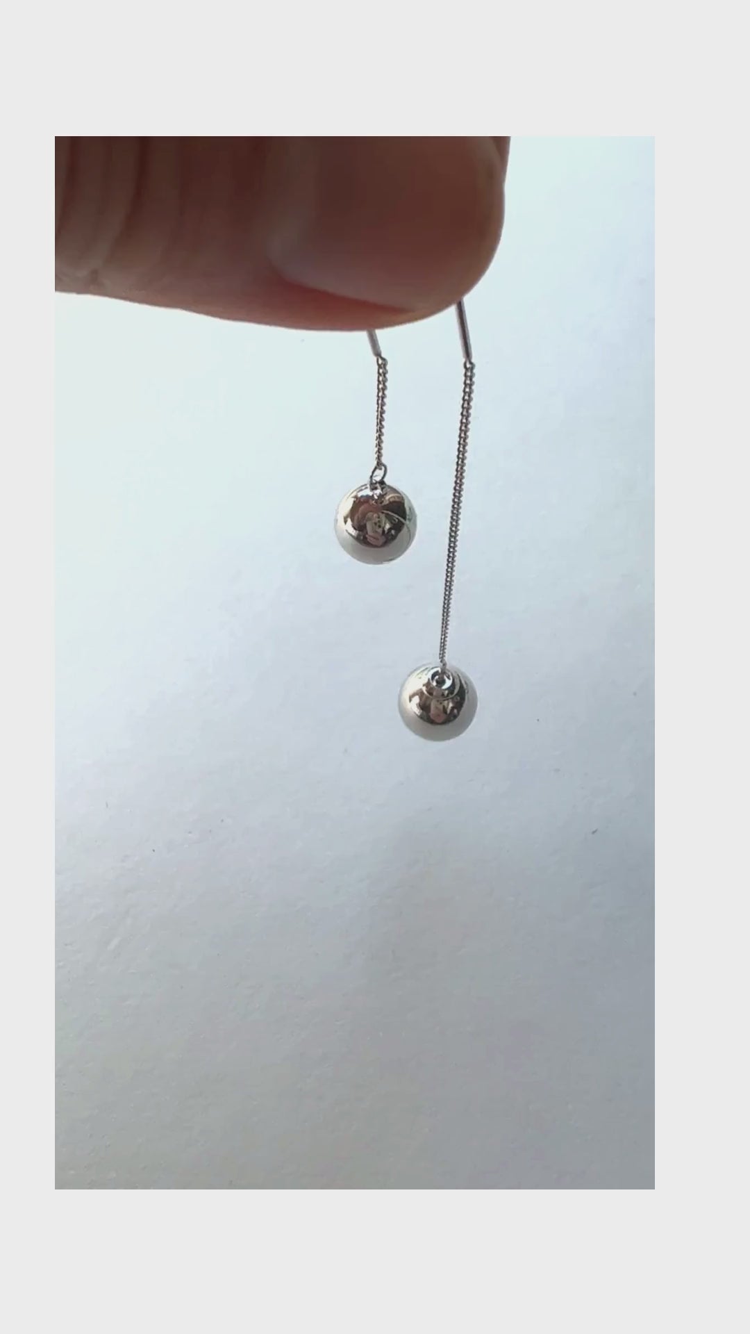 Two balls are suspended from a chain and appear to balance. The ball (on the longer chain) is removable so you can put on the earring and then reattach then end. 